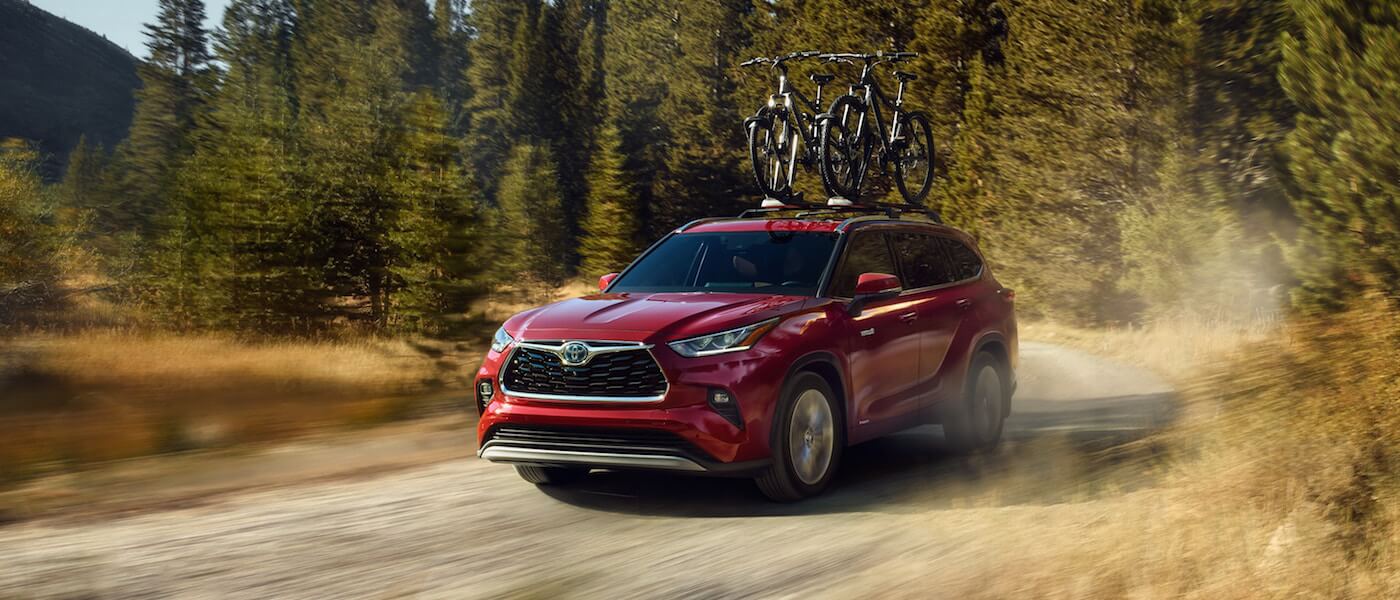 A red 2020 Toyota Highlander Hybrid carrying bikes down an open road