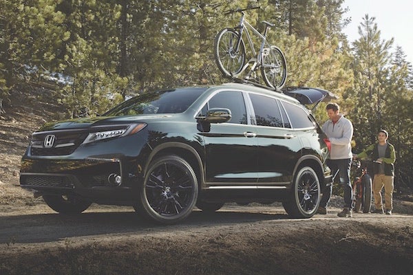 A green 2019 Honda Pilot with bikes on top in the forest