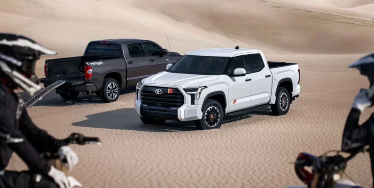 Two Toyota trucks parked side by side in a vast desert landscape under a clear blue sky.