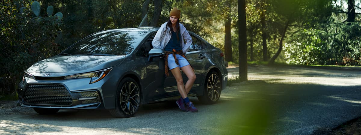 A woman leaning against her 2020 Toyota Corolla