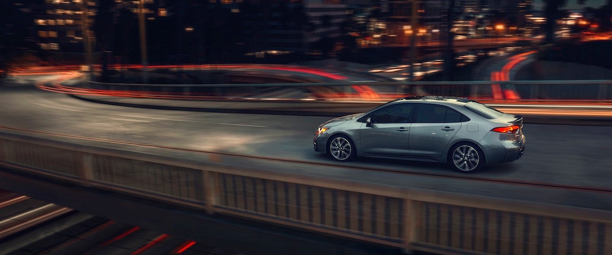A silver 2020 Toyota Corolla driving through a city at night